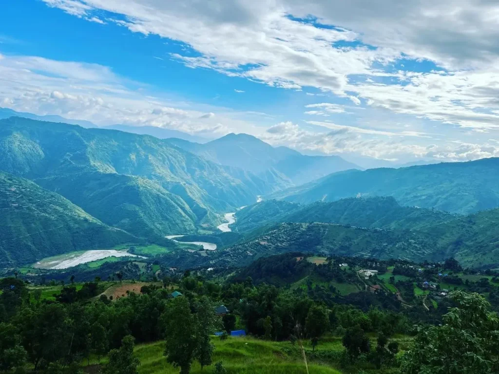 Scenic view of lush green hills and a winding river under a bright blue sky in Okhaldhunga, Nepal.